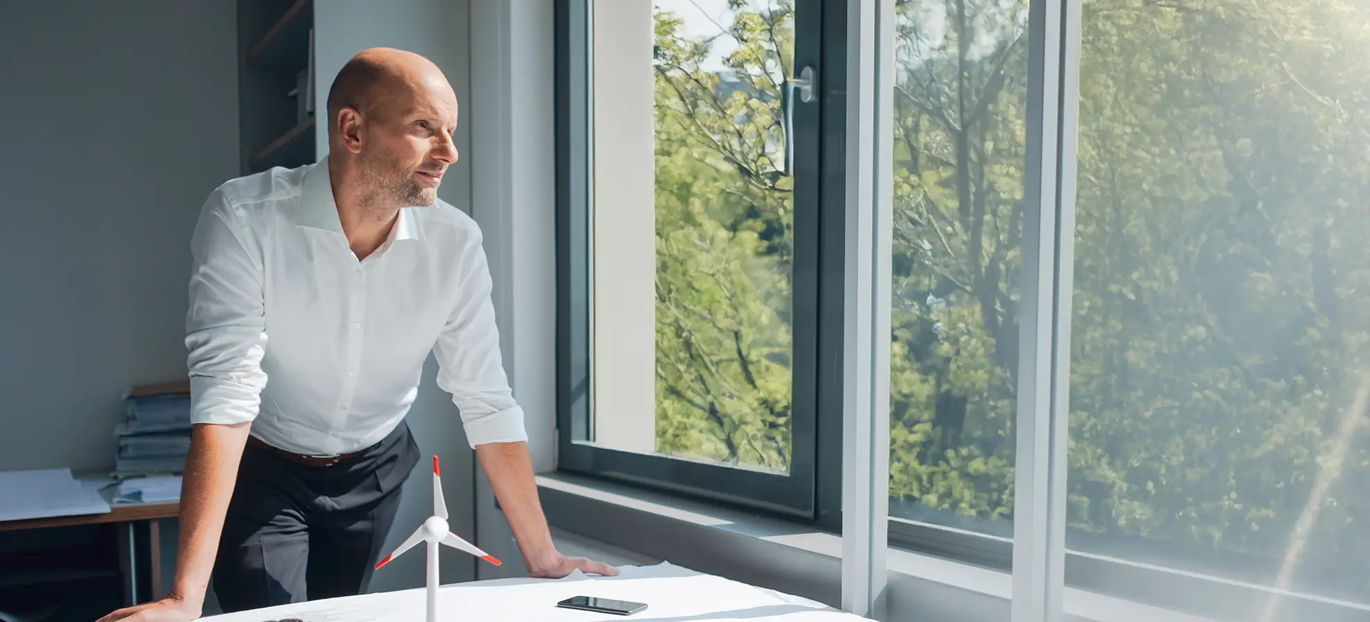 Mann steht vor Schreibtisch und blickt aus dem Fenster ins Grüne.